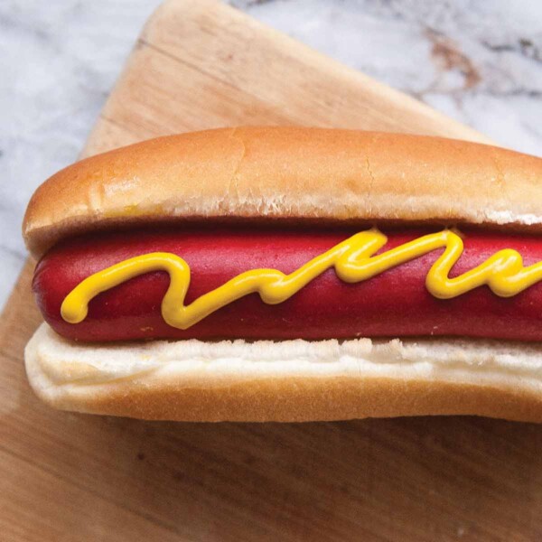 A perfect hot dog in a white bun, topped with a squiggle of mustard.