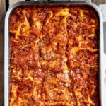 A metal baking dish filled with the Pioneer Woman's favorite lasagna on a wooden table.