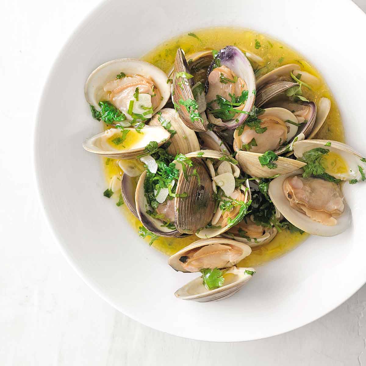 A white bowl of Portuguese clams with vinho verde in a olive oil and garlic sauce, garnished with cilantro.