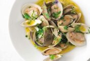 A white bowl of Portuguese clams with vinho verde in a olive oil and garlic sauce, garnished with cilantro.