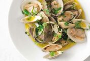 A white bowl of Portuguese clams with vinho verde in a olive oil and garlic sauce, garnished with cilantro.