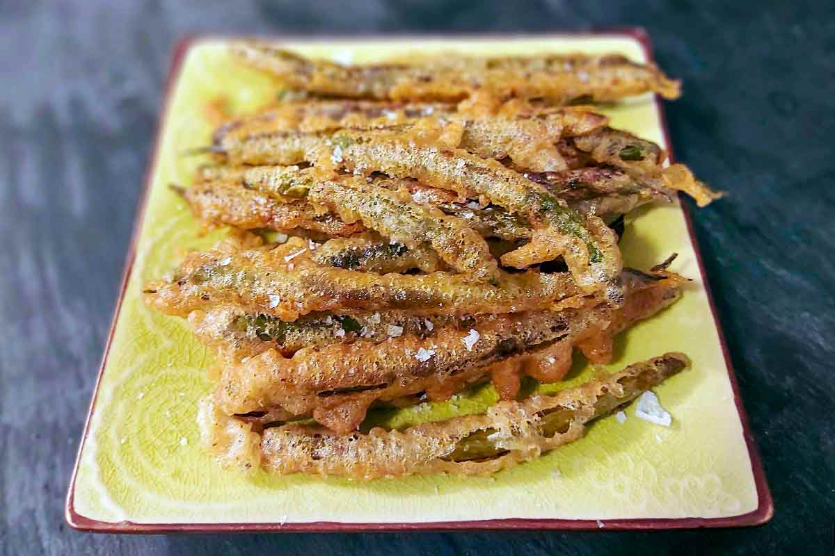 Portuguese deep-fried green beans piled on a rectangular platter, sprinkled with flaky salt.
