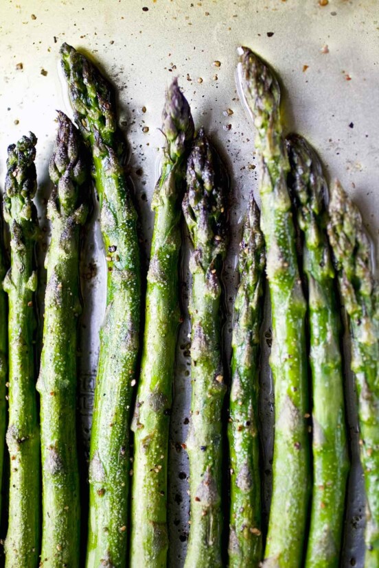 Ten spears of asparagus seasoned with salt and pepper and arranged in a row on a baking sheet.