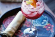 A glass of ruby sangria with a skewer of fruit suspended over the glass on a floral serving tray.
