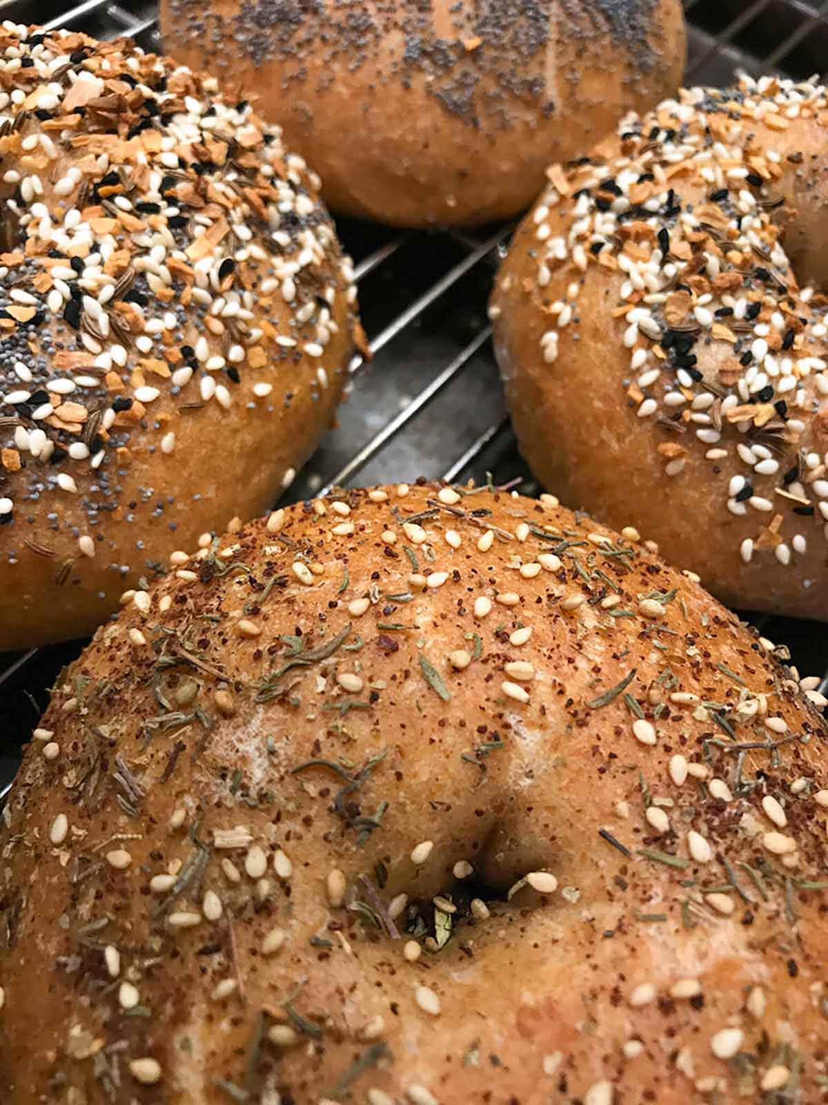 Rye bagels topped with assorted spices on a wire rack.