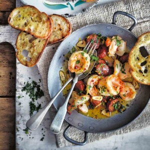 A skillet filled with shrimp with chorizo and toasted bread slices on the side.
