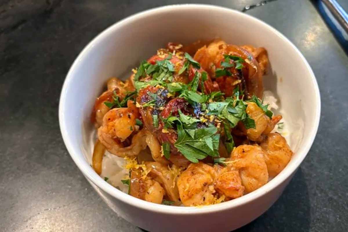 A white bowl filled with rice and topped with shrimp and chouri&ccedil;o in a garlicky lemony sauce.