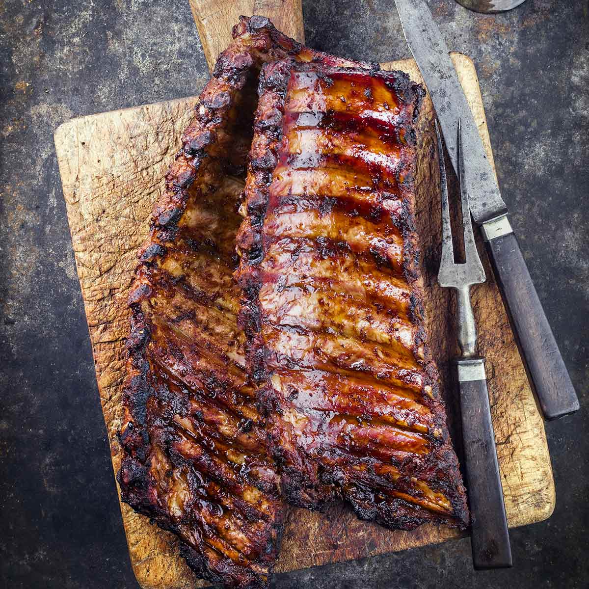 A wooden cutting board topped with two rack of smoked pork ribs.