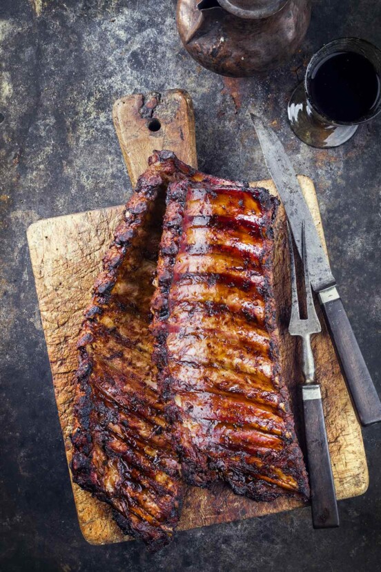 A wooden cutting board topped with two rack of smoked pork ribs.