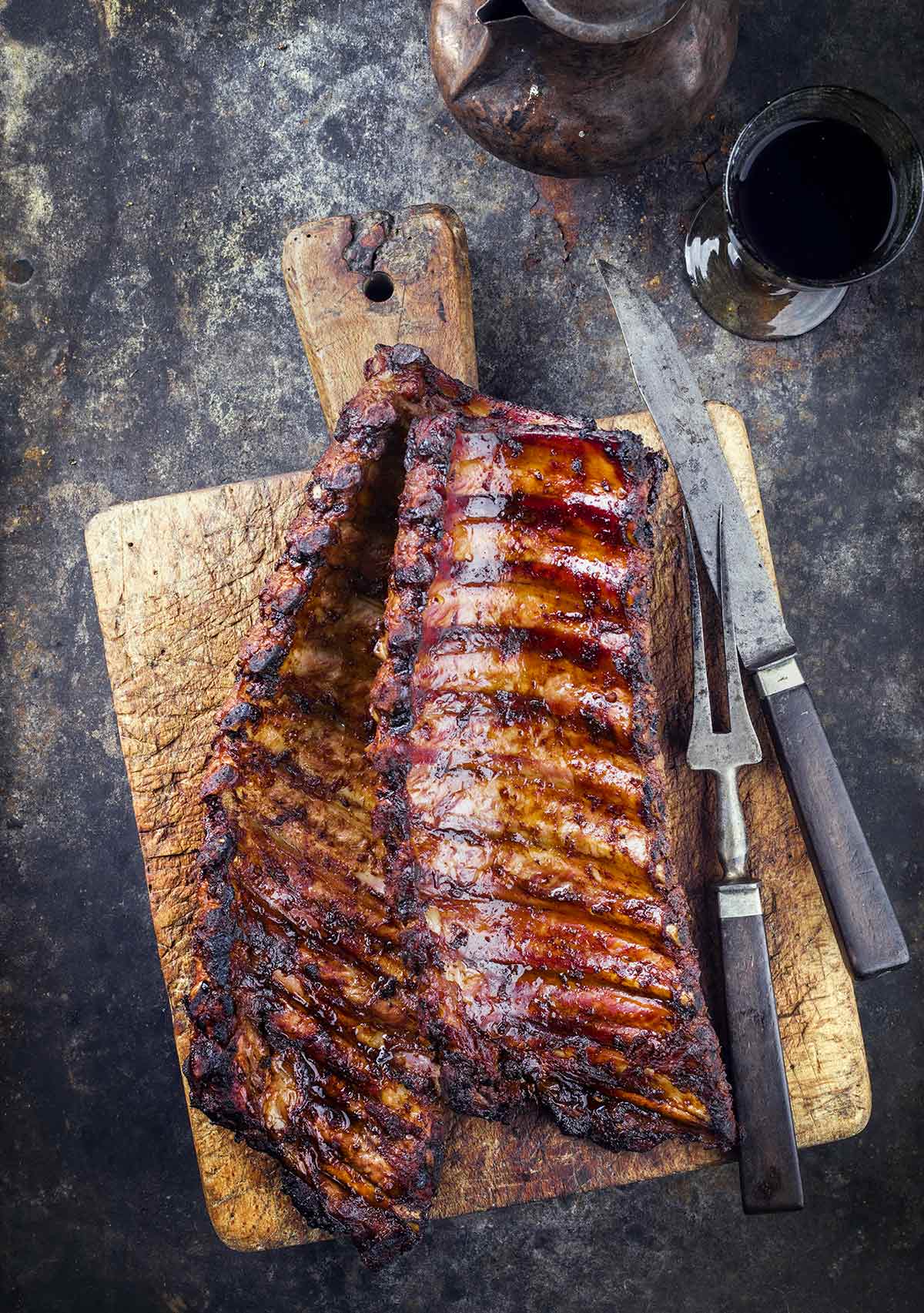 A wooden cutting board topped with two rack of smoked pork ribs.