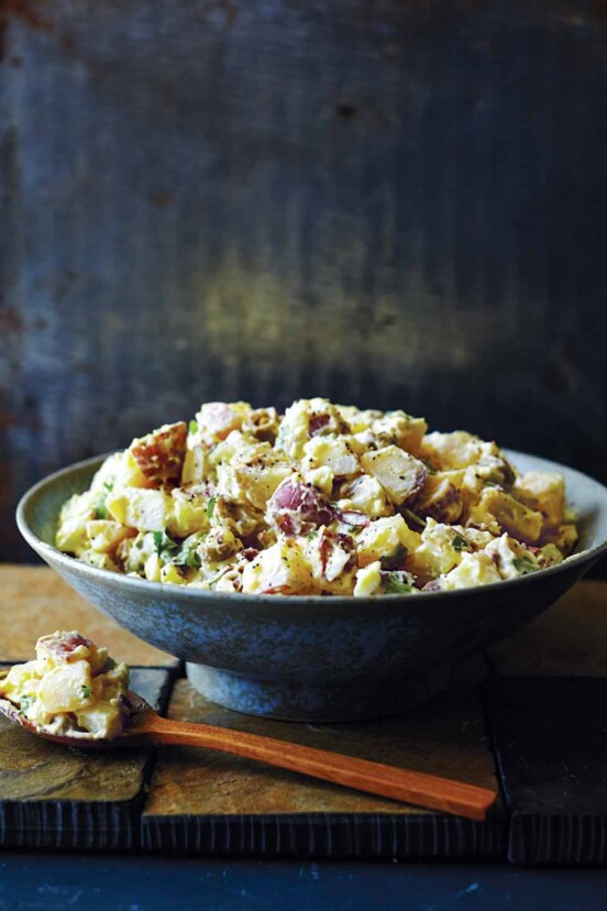 A bowl filled with Southern potato salad with a wooden spoon ad a scoop of salad on the side.