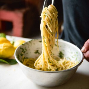 A person using metal chopsticks to scoop up spaghetti al limone amalfitano from a bowl.