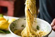 A person using metal chopsticks to scoop up spaghetti al limone amalfitano from a bowl.