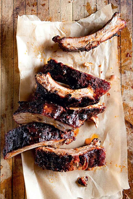 Seven spice-rubbed baby back ribs on a piece of parchment on a wooden surface.
