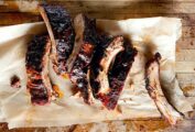 Seven spice-rubbed baby back ribs on a piece of parchment on a wooden surface..