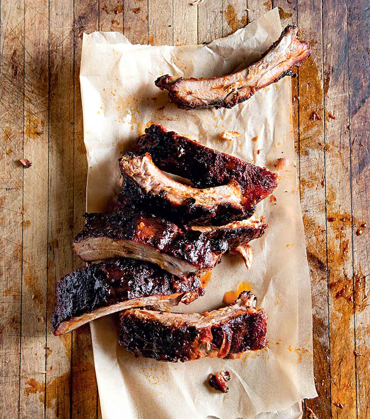 Seven spice-rubbed baby back ribs on a piece of parchment on a wooden surface.