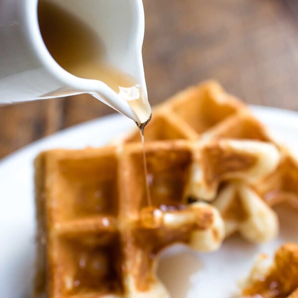 Spicy bourbon maple syrup being poured over waffles from a white pitcher.