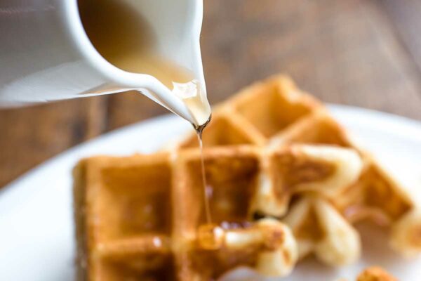 Spicy bourbon maple syrup being poured over waffles from a white pitcher.