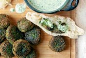 Spinach falafel on a cutting board with some tucked into a pita, and a bowl of parsley tahini sauce.