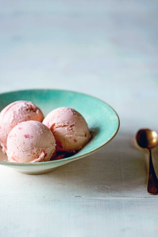 A blue bowl with three scoops of strawberry buttermilk ice cream and a gold spoon on the side.