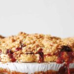A strawberry rhubarb pie with ginger crumb topping with some filling oozing from the pie.
