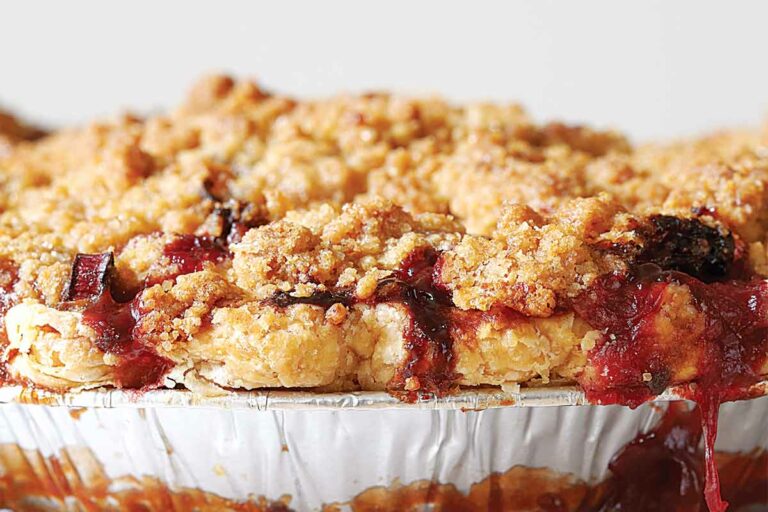 A strawberry rhubarb pie with ginger crumb topping with some filling oozing from the pie.