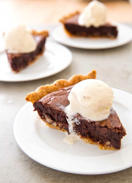 Slices of tar heel pie on individual white plates, each topped with a scoop of vanilla ice cream.
