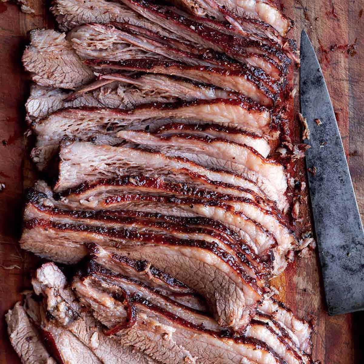 A sliced Texas brisket on a wooden board with a knife lying beside it.