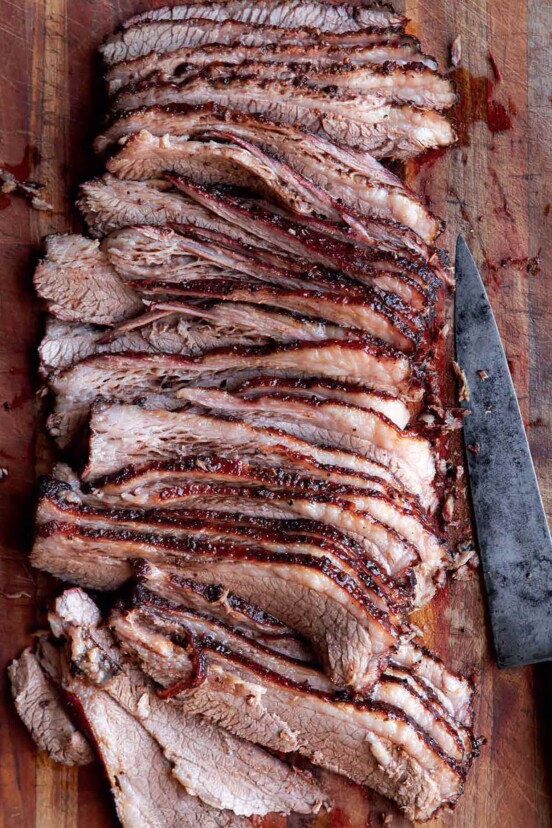 A sliced Texas brisket on a wooden board with a knife lying beside it.