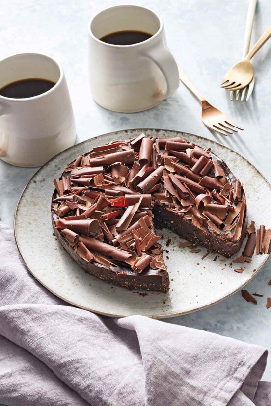 Two mugs of coffee and a white plate with a vegan no-bake fudge cake