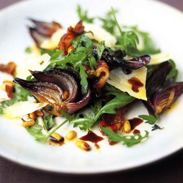 A plate of warm arugula salad -- caramelized red onions, arugula, shaved Parmesan, and toasted pine nuts with a balsamic drizzle.