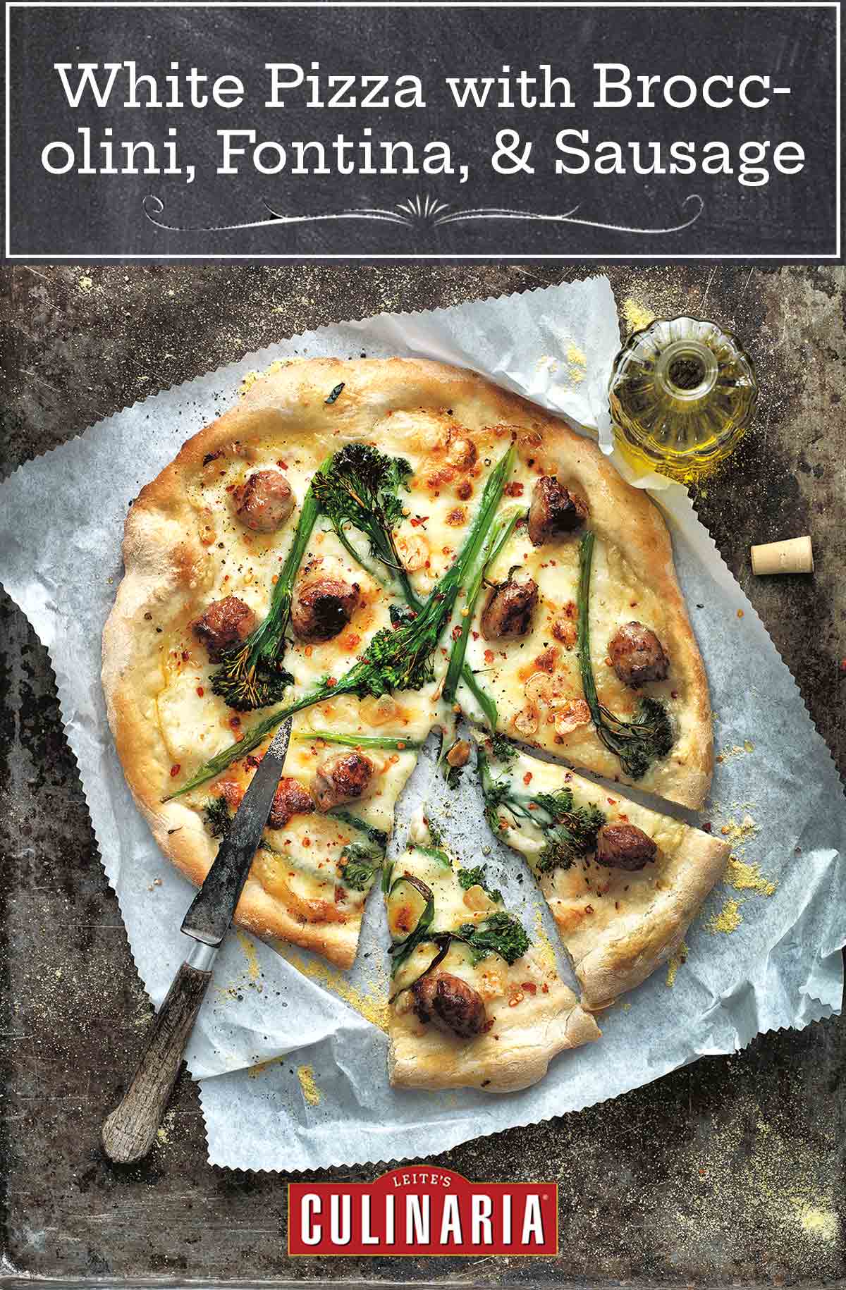A white pizza with broccolini, fontina, and sausage cut into slices on a piece of parchment with a knife on top and a bottle of oil on the side.