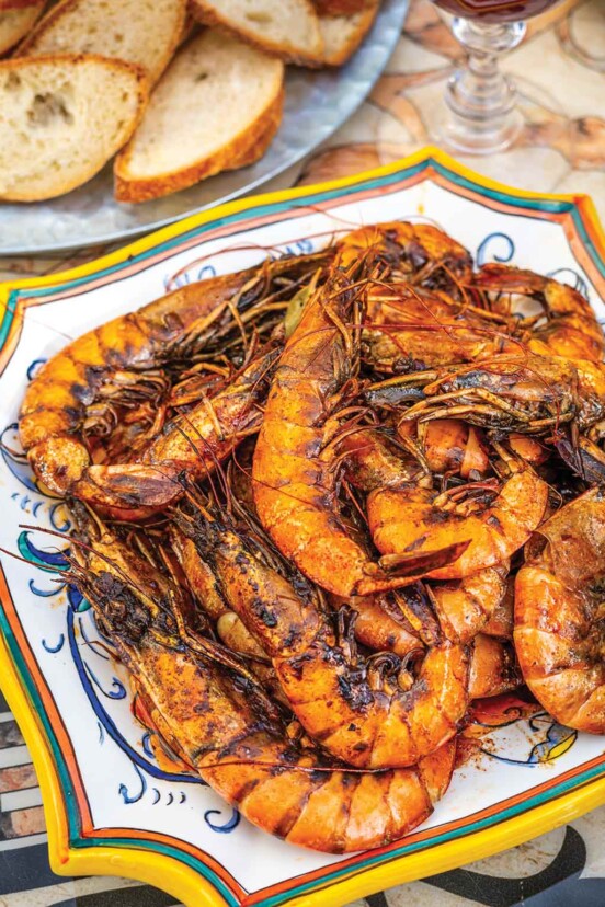 A platter of baked shrimp with Creole sauce with bread slices on the side.