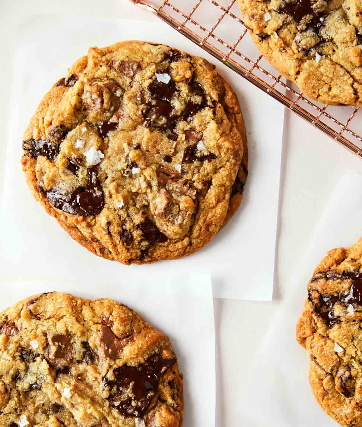 Several bakery style chocolate chip cookies cooling on a rack.