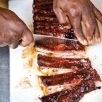 A person cutting a slab of the best St. Louis ribs into individual ribs.