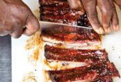 A person cutting a slab of the best St. Louis ribs into individual ribs.