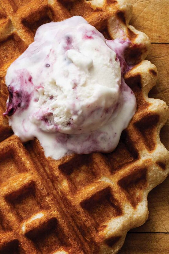 A scoop of black currant ice cream melting over a waffle.