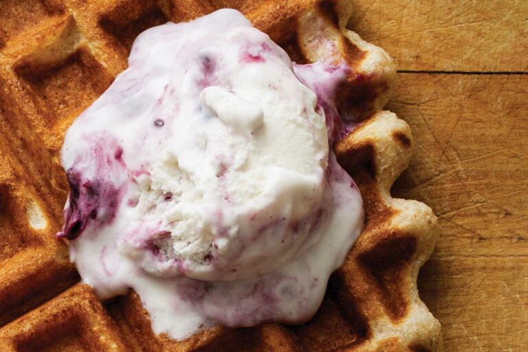 A scoop of black currant ice cream melting over a waffle.