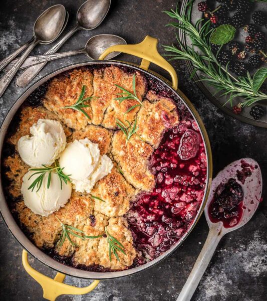 A Blackberry Ginger Slump With Rosemary Dumplings in a yellow pot with scoops of vanilla ice cream