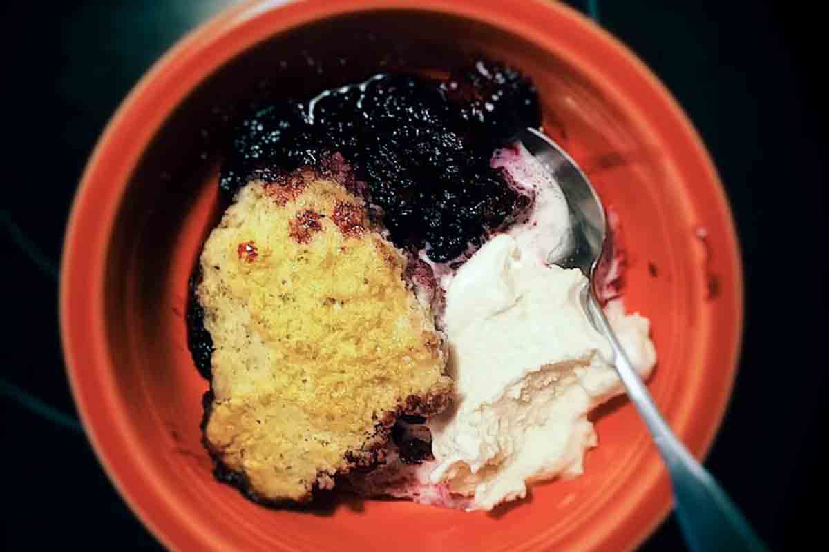A Blackberry Ginger Slump With Rosemary Dumplings in a red bowl with scoops of vanilla ice cream