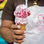 A person holding an ice cream cone with 2 scoops of blackberry ice cream.
