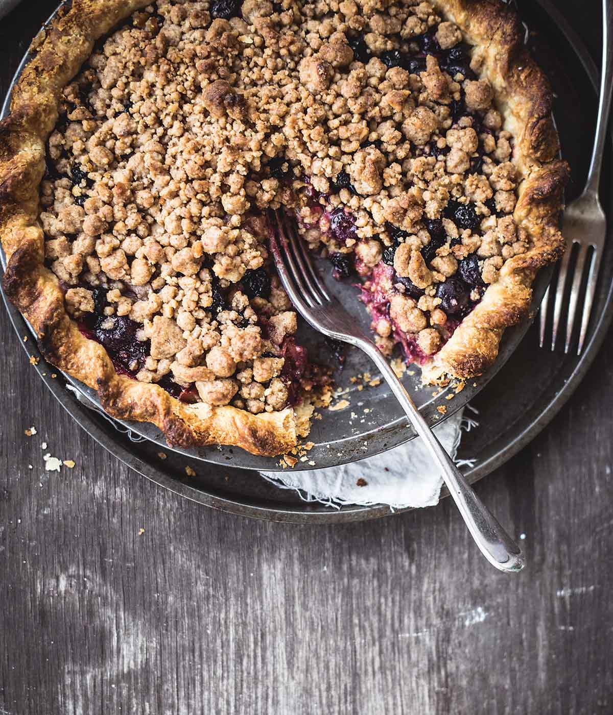 A bluebarb pie with one slice missing and two forks resting beside the blueberry and rhubarb pie.