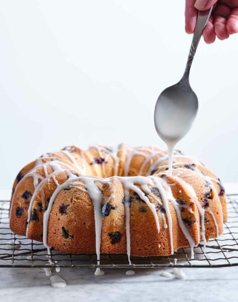 Blueberry coffee cake on a cooling rack with a spoon drizzling icing over it.