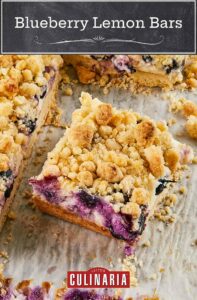 A sheet of blueberry lemon bars with one cut out, laying on a piece of parchment paper.