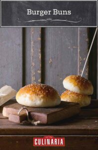 Three burger buns topped with sesame seeds on a wooden surface.