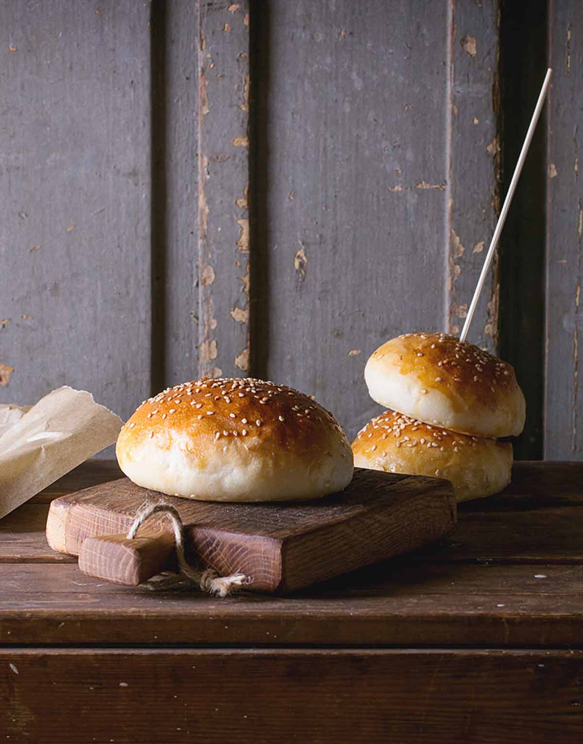 Three burger buns topped with sesame seeds on a wooden surface.