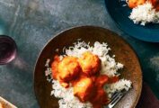 A plate topped with white rice and three chicken tikka masala meatballs with a fork on the side.