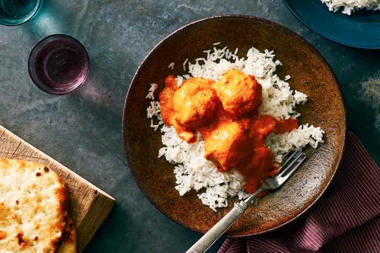 A plate topped with white rice and three chicken tikka masala meatballs with a fork on the side.