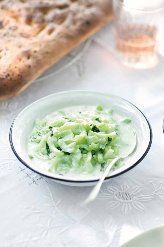 A bowl of chilled cucumber soup with a spoon resting inside.