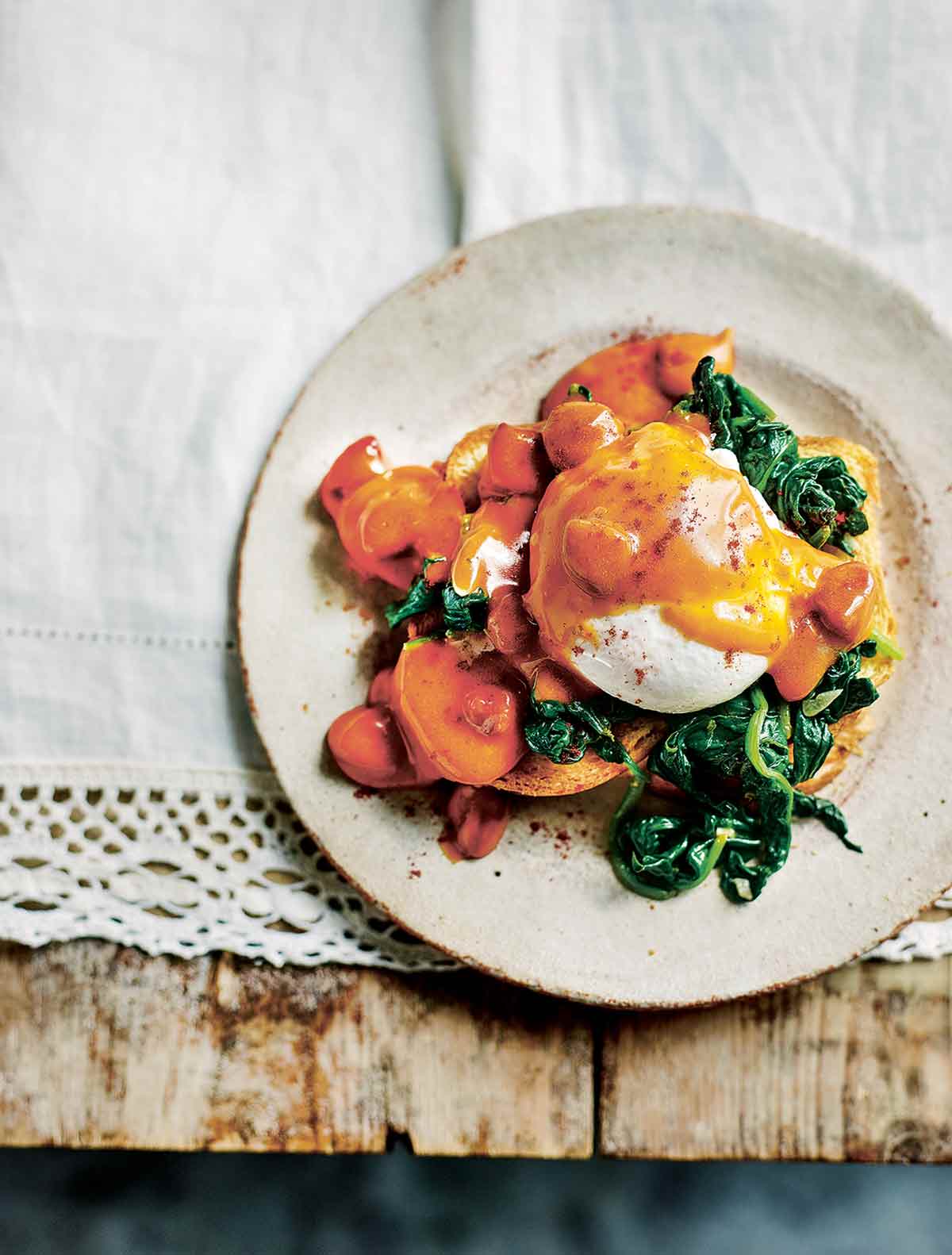 A plate topped with a serving of chorizo eggs benedict - chorizo hollandaise, garlicky spinach, and poached egg on toast.